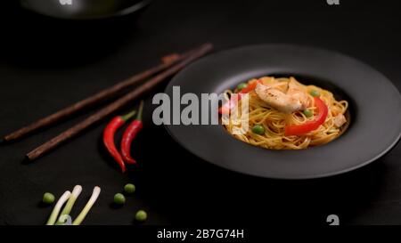 Shopped shot di Schezwan Noodles o Chow Mein con verdure e pollo in piatto nero su tavolo nero Foto Stock