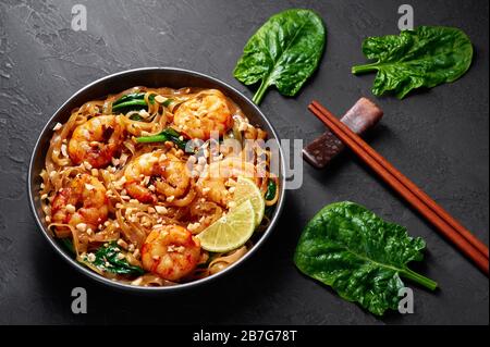 Gamberi Pad vedere EW in ciotola nera su sfondo ardesia scuro. Il pad See EW è un piatto di cucina tailandese con tagliatelle di riso, gamberi, salsa di soia e ostriche e verdure. Foto Stock