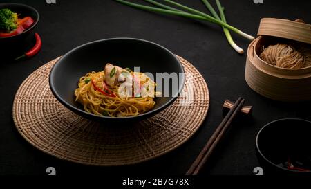 Espresso di Schezwan Noodles o Chow Mein con verdure, pollo e salsa di peperoncino serviti in ciotola nera e ingredienti su tavola nera Foto Stock