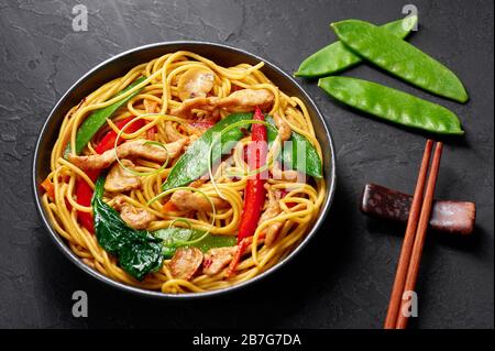 Pollo lo Mein in ciotola nera su sfondo ardesia scuro. Lo Mein è un piatto di cucina cinese con carne di pollo, tagliatelle d'uovo, verdure e salse. Cinese Foto Stock