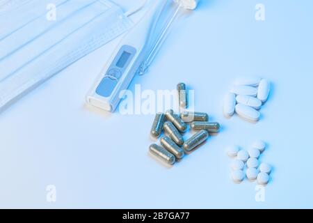 termometro elettronico, maschera protettiva e compresse le pillole giacciono su uno sfondo bianco con illuminazione blu Foto Stock