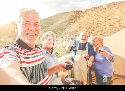 Buon senior amici prendere selfie a barbecue cena in affitto villa con vista montagna - pensionati che si divertono con le tendenze della tecnologia - gioioso Foto Stock