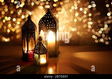 Lanterne arabe ornamentali con scintillanti luci bokeh. Le candele bruciate sul tavolo si illuminano di notte. Biglietto di auguri per le feste, invito per i musulmani Foto Stock