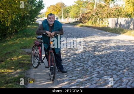 Ritratto di contadino ucraino seanior in piedi con antica bicicletta su una strada acciottolata ancien Foto Stock