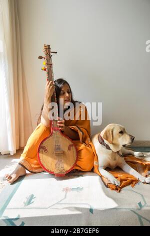 Cane seduto accanto al suo proprietario, mentre la donna che suona la musica sul suo tambura. Foto Stock