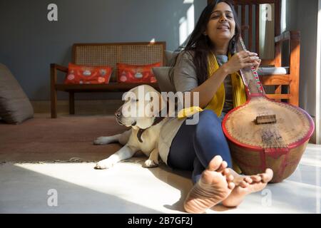 Donna seduta con il suo cane mentre suona la musica sulla sua tambura e cantare. Foto Stock