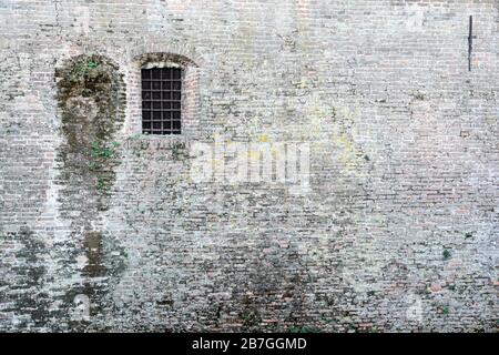 Antico muro di mattoni e una finestra bloccata con barre di metallo Foto Stock