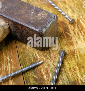 Vecchio martello arrugginito e tre chiodi in acciaio giacciono su una tavola di legno graffiata. Spazio di copia per il testo. Messa a fuoco selettiva. Concetto di lavoro domestico. Formato quadrato. Chiudi- Foto Stock