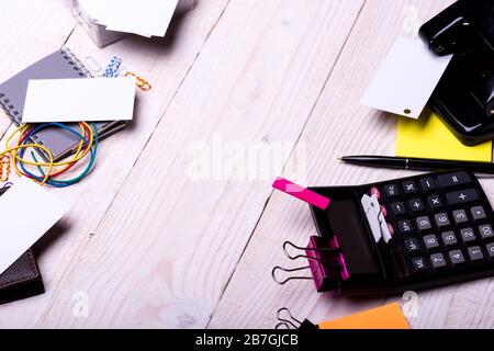 Schede vicino a notebook, portafoglio, clip e penna su sfondo di legno bianco. Perforatore, elastici, spille e leganti vicino a foglietti adesivi gialli. Idee e accessori per il business. Cancelleria e calcolatrice. Foto Stock