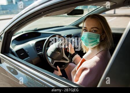 Donna in maschera protettiva alla guida di un'auto su strada. Viaggi sicuri. Foto Stock