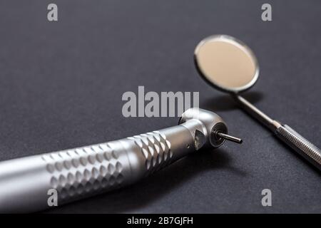 Manipolo odontoiatrico ad alta velocità e specchio metallico. Strumenti dentali per il trattamento dentale su sfondo nero. Strumenti medici. Vista ravvicinata. Profondità poco profonda Foto Stock