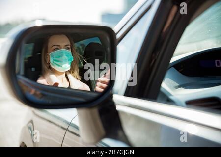 Donna in maschera protettiva alla guida di un'auto su strada. Viaggi sicuri. Foto Stock