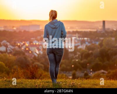 Vista posteriore della donna che gode di un bellissimo tramonto con la città di Augusta sullo sfondo Foto Stock