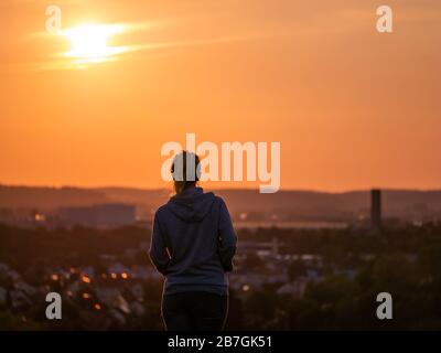 Vista posteriore della donna che gode di un bellissimo tramonto con la città di Augusta sullo sfondo Foto Stock