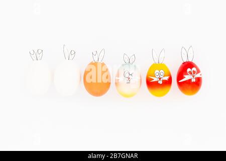Uova di pasqua bianche, marroni e colorate dipinte con divertenti orecchie di coniglietto e facce di cartoni animati su sfondo bianco Foto Stock