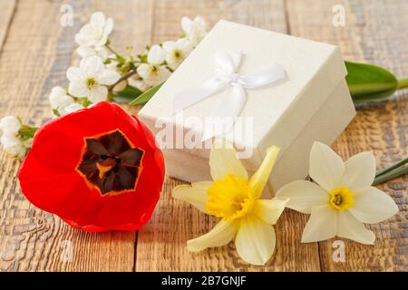 Scatola regalo decorata con fiori di tulipano, narcisi e gelsomino su tavole di legno. Foto Stock