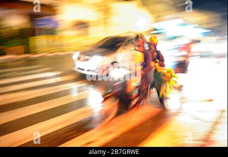 Moto pesante con due persone nel traffico notturno in città asiatica. Sfocatura del movimento. Foto Stock