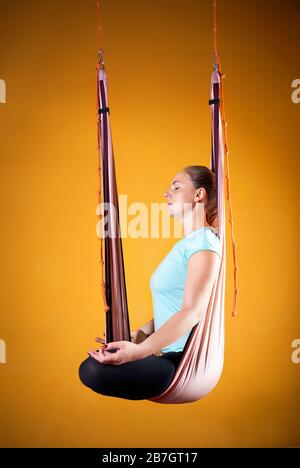 Giovane donna facendo antigravity yoga posizione meditativa a sfondo giallo Foto Stock