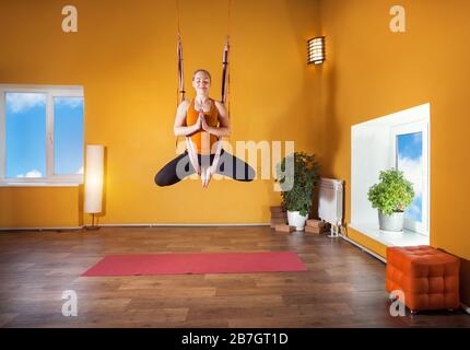 Giovane donna facendo antigravity yoga posizione meditativa presso lo studio con pareti di colore giallo Foto Stock