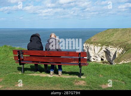 Coppia seduta su panchina, North Landing, Flamborough Head, East Yorkshire, Inghilterra Regno Unito Foto Stock