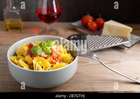 Tortellini fatti in casa con salsa di pomodoro arrabbiata e formaggio con un bicchiere di vino sul lato. Foto Stock