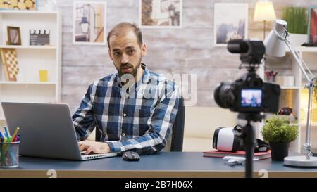 Famoso giovane vlogger digitando su laptop mentre parla con i suoi abbonati su un podcast. Contenuto creativo creatore. Foto Stock