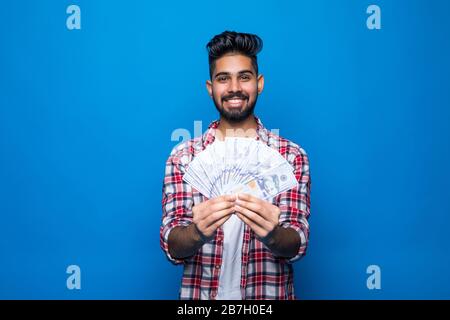 Ritratto di bel giovane uomo che mostra banconote in piedi su sfondo blu Foto Stock