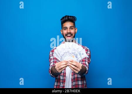 Ritratto di bel giovane uomo che mostra banconote in piedi su sfondo blu Foto Stock