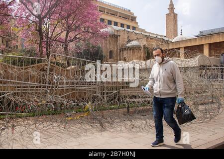 Beirut, Libano. 16 marzo 2020. Un pedone che indossa una maschera protettiva contro il covid 19 romanzo coronavirus cammina oltre una barricata di spinato e filo di rasoio che protegge il Parlamento libanese come il Libano annuncia due settimane di blocco su coronavirus Credit: amer Ghazzal/Alamy Live News Foto Stock