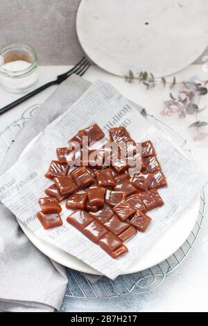 Caramelle salate tagliate a pezzi quadrati, vista dall'alto su carta da forno grigia e piastra bianca Foto Stock