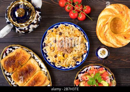 Pilaf nazionale uzbeko con carne, insalata di achichuk di pomodoro, cetriolo, cipolla in piatto con modello tradizionale, coriandolo, pomodori ciliegini, panpepato Foto Stock