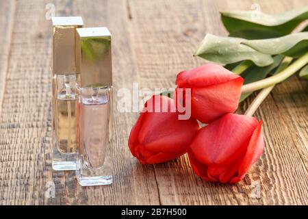 Bottiglie di profumo e tulipani rossi su tavole di legno. Foto Stock