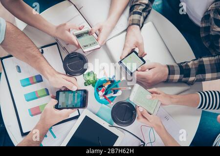 Fai il giro di quattro amici che usano i loro smartphone per cercare idee per un nuovo business di successo in un ambiente di lavoro seduto al tavolo Foto Stock