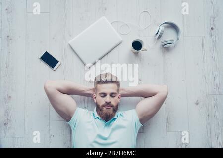 Vista dall'alto di un uomo calmo in un abbigliamento casual disteso sul pavimento e riposante dopo il lavoro Foto Stock