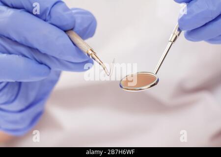 Vista ravvicinata delle mani del dentista nei guanti in lattice con sonda e specchio per la bocca. Profondità di campo bassa. Concetto di strumenti medici. Foto Stock