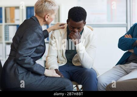 Ritratto di giovane afro-americano che piange mentre si siede sulla sedia in gruppo di sostegno cerchio, copia spazio Foto Stock