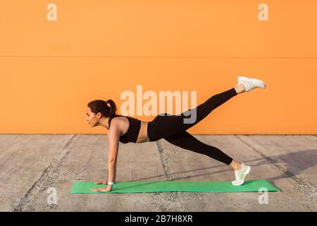 Giovane donna atletica sottile in abbigliamento sportivo, pantaloni neri e top, yoga pratica, in piedi in Phalakasana più alta posa in piedi con sollevamento gambe, muscl allenamento Foto Stock