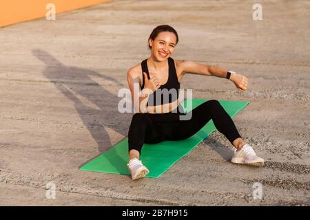 Gioiosa ragazza atletica sorridente che mostra orologio da polso, fitness tracker a portata di mano, e la gesturing pollici in su, soddisfatti con indicatori di salute dopo gli allenamenti, s Foto Stock