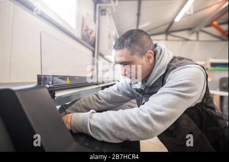 L'operatore tecnico elettrico ripara una stampante industriale di alta qualità e una macchina plotter di grandi dimensioni nell'ufficio della tipografia digitale Foto Stock