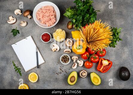 Verdure e ingredienti diversi per la preparazione della pasta. Un libro per la scrittura delle ricette si trova sulla tabella. Spazio di copia per il testo Foto Stock