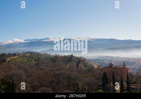 Bella fotografia di paesaggio di Granada, Andalusia, Spagna che mostra parti della città in foschia e nebbia con le montagne della Sierra Nevada sul retro Foto Stock