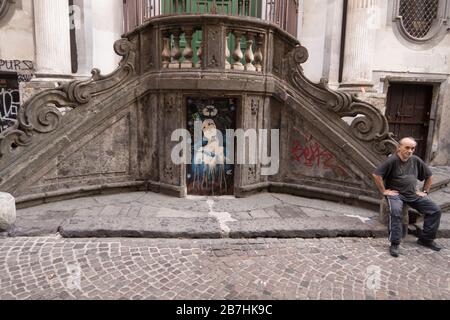 Un uomo seduto accanto a un graffito di una Vergine Maria con un simbolo di riciclaggio sopra la testa nel centro di Napoli, Italia. Foto Stock