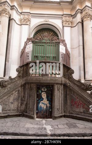 Un graffito di una Vergine Maria con un simbolo di riciclaggio sopra la testa su una porta sul fondo di una scalinata di fronte ad una chiesa di Napoli, Italia. Foto Stock