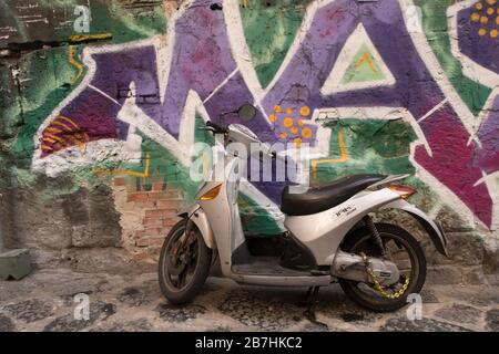 Uno scooter parcheggiato contro un muro ricoperto di graffiti in una strada di Napoli Foto Stock