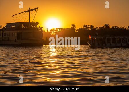 Il sole sorge sul fiume Nilo a Luxor con silhouette di traghetti Foto Stock