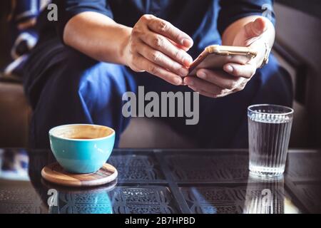 Imprenditore utilizza lo smartphone per leggere notizie di investimento e mail di risposta a conferma riunione in coffee shop. l uomo di bere latte caffè prima di andare a lavorare Foto Stock