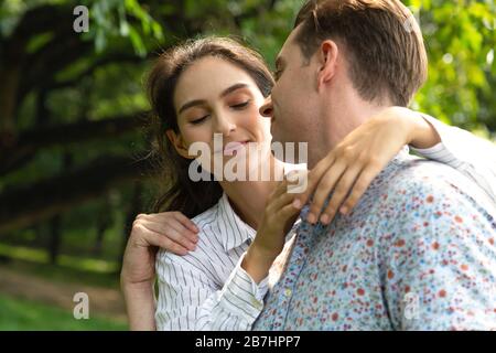 primo piano bella giovane coppia romantico uomo e donna abbracciando faccia a faccia sorridendo e chiudendo gli occhi prima di baciare mentre datando nel parco nella somma Foto Stock