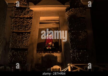 Una statua di Gesù è incorniciata da ossa e teschi al Cimitero delle Fontanelle di Napoli Foto Stock