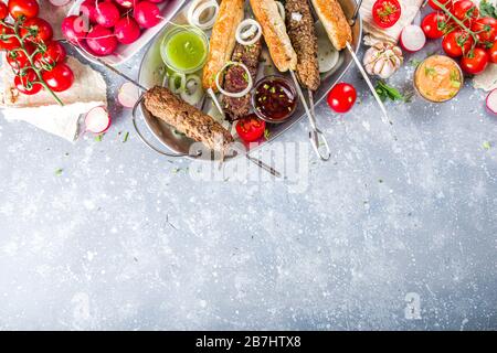 Festa estiva al barbecue. Shish kebab su un bastone, da macinato di carne di manzo e di pollo. Lula kebab, piatto tradizionale caucasico asiatico. Con varie salse, spezie Foto Stock