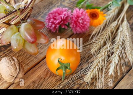 Primo piano pomodoro giallo, noci, uva, orso di grano, fiore di calendula e cesto di vimini su vecchie tavole di legno. Profondità di campo bassa. Vista dall'alto. Foto Stock
